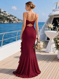 Back view of a burgundy chiffon floor-length bridesmaid dress with spaghetti straps, bow open back detail, center back zipper, cascading side ruffle, and flowing mermaid-style skirt.