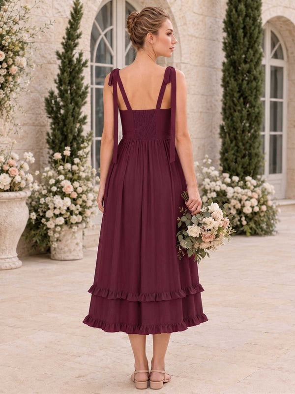 Back view of a burgundy chiffon midi bridesmaid dress with tie shoulder straps, shirred back bodice, fitted waist, flowing A-line skirt, and tiered ruffle hem.
