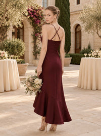 Back view of a burgundy satin midi bridesmaid dress with slim spaghetti straps, crisscross back detail, fitted silhouette, and softly flared asymmetrical mermaid hem.