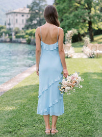Back view of a light blue chiffon midi bridesmaid dress with slim spaghetti straps, low back, soft back ruffle detail, asymmetrical cascading ruffles, and elegant flowing A-line silhouette.