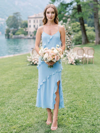 Front view of a light blue chiffon midi bridesmaid dress with V-neckline, spaghetti straps, cascading asymmetrical ruffle detail, front slit, and flowing A-line skirt.