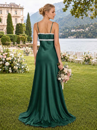 Back view of an emerald satin floor-length bridesmaid dress with spaghetti straps, gathered upper-back panel, ivory lace trim, fitted bodice, and softly flowing fit-and-flare skirt.