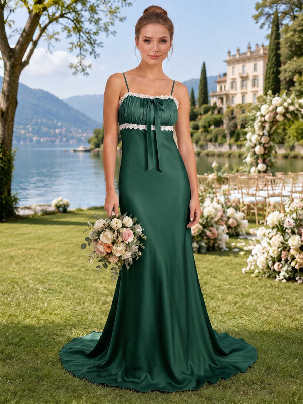 Front view of an emerald satin floor-length bridesmaid dress with square neckline, spaghetti straps, gathered bust, ivory lace trim, tie-front detail, and flowing fit-and-flare skirt.