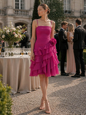 Front view of a fuchsia chiffon tea-length bridesmaid dress featuring slim spaghetti straps, a straight neckline, finely ruched fitted bodice, asymmetrical waistline, statement floral hip accent, and cascading layered ruffle skirt.