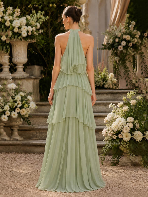 Back view of a sage green chiffon floor-length bridesmaid dress featuring an open-back halter neckline, cascading chiffon layers from the neck, tiered ruffle detailing through the waist and skirt, and a flowing A-line silhouette.