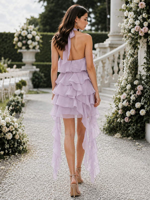 Back view of a lilac chiffon high-low bridesmaid dress featuring an open-back halter design with a long neck tie, softly layered back ruffles, tiered asymmetric skirt, and elongated cascading chiffon panels at both sides.