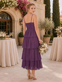 Back view of a plum chiffon tea-length bridesmaid dress featuring slim spaghetti straps, a smocked back bodice, fitted waist, and flowing layered tiered ruffle skirt.