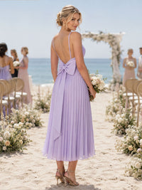 Back view of a lilac chiffon midi bridesmaid dress featuring slim spaghetti straps, a low open back, statement bow at the waist, finely pleated A-line skirt, and softly flowing midi hem.