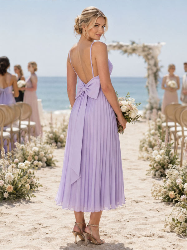 Back view of a lilac chiffon midi bridesmaid dress featuring slim spaghetti straps, a low open back, statement bow at the waist, finely pleated A-line skirt, and softly flowing midi hem.