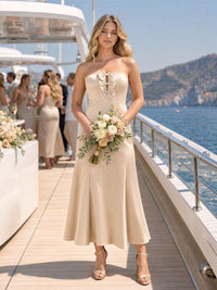 Front view of a champagne imitation silk bridesmaid dress featuring a strapless neckline, bow-trimmed front bodice detail, fitted waist, elegant fit-and-flare silhouette, and tea-length flared hem.