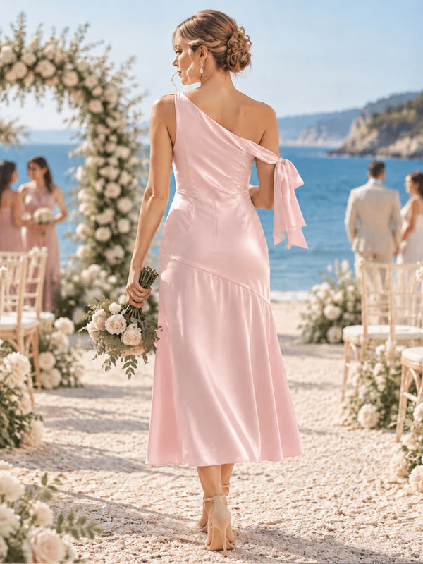 Back view of a light pink imitation silk bridesmaid dress featuring a one-shoulder back design, shoulder bow detail, fitted bodice, softly flared tea-length skirt, and elegant asymmetrical silhouette.