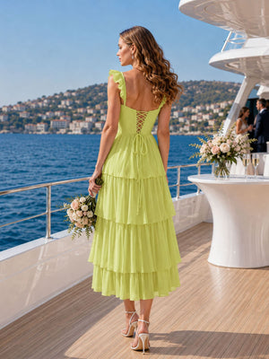 Back view of a pale lime chiffon bridesmaid dress featuring ruffle straps, a lace-up back, back bow tie detail, fitted bodice, and a tiered tea-length A-line skirt.