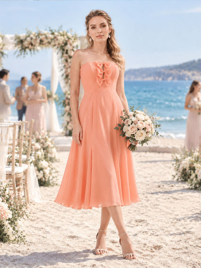Front view of a soft apricot chiffon bridesmaid dress featuring a strapless neckline, vertical bow-trimmed bodice detail, fitted waist, flowing A-line silhouette, and elegant tea-length skirt.