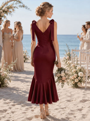 Back view of a burgundy imitation silk bridesmaid dress featuring a V-back neckline, shoulder bow straps with ribbon tails, fitted waist, concealed center-back zipper, and tea-length flared mermaid hem.