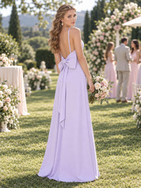 Back view of a lilac chiffon bridesmaid dress featuring a low open back with spaghetti straps, statement back bow with long tails, fitted waist, and floor-length sheath silhouette.
