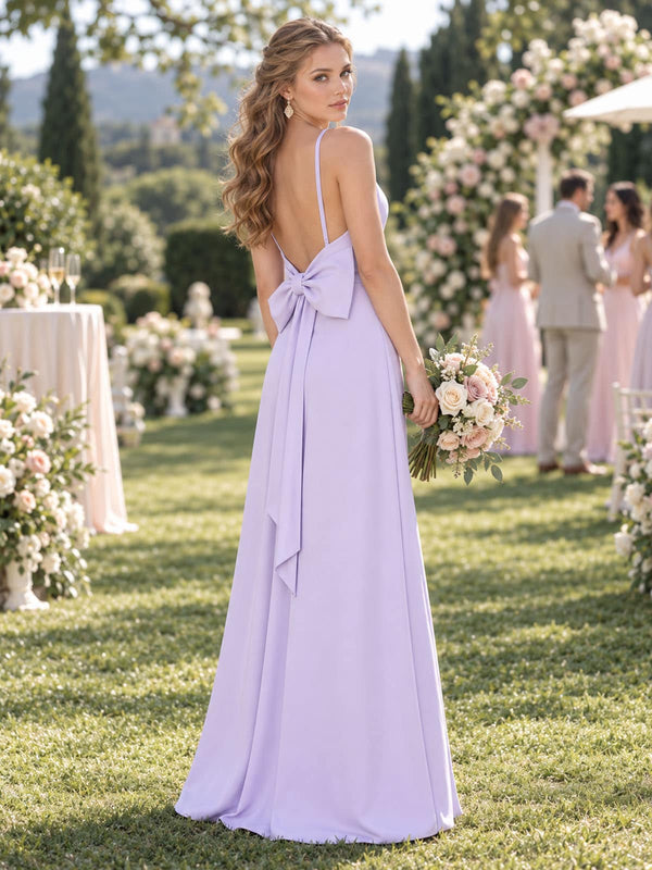 Back view of a lilac chiffon bridesmaid dress featuring a low open back with spaghetti straps, statement back bow with long tails, fitted waist, and floor-length sheath silhouette.