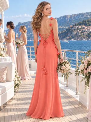 Back view of a coral chiffon bridesmaid dress featuring floral-appliqué spaghetti straps, a low open back, adjustable lace-up detailing, long tie ends with floral accents, and a flowing floor-length sheath silhouette.