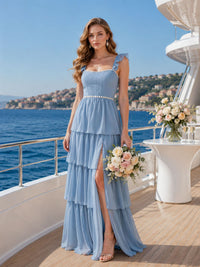Front view of a light blue chiffon bridesmaid dress featuring a square neckline, ruffle straps, ruched bodice, defined waist trim, layered tiered floor-length skirt, and elegant side slit.
