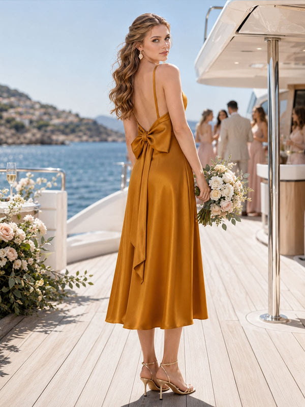 Back view of a Golden Ochre imitation silk bridesmaid dress featuring delicate spaghetti straps, a low open back, statement bow detail at the back waist with long flowing bow tails, and an elegant tea-length skirt.
