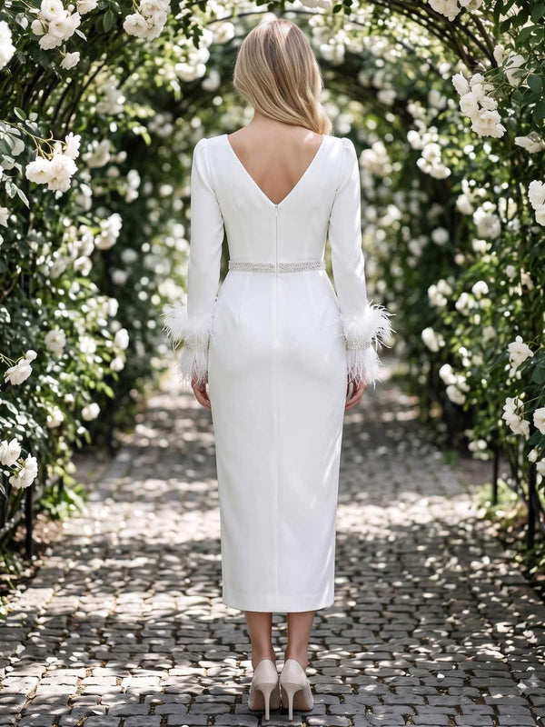 White satin mother of the bride dress back view with deep V-back, long sleeves, feather cuffs, embellished waist detail, concealed back zipper, and tea length skirt