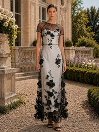 Floral tulle mother of the bride dress front view with illusion neckline, sheer short sleeves, black floral lace appliques, satin base, and floor length sheath skirt