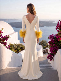 Back view of an ivory satin floor-length mother of the bride dress with deep V-back neckline, long fitted sleeves, bright yellow feather-trim cuffs, waist belt, center-back zipper, fitted silhouette, and softly flared mermaid hem.