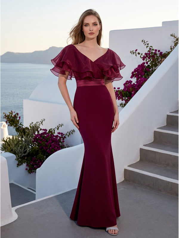 Front view of a burgundy satin floor-length mother of the bride dress with V-neckline, layered organza ruffle cape sleeves, satin waistband, fitted bodice, and softly flared mermaid skirt.