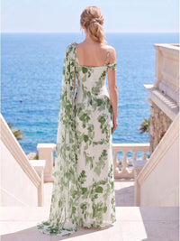 Back view of a floral chiffon floor-length mother of the bride dress with an asymmetrical one-shoulder construction, long draped cape extending from the embellished shoulder, fitted back silhouette, and center-back zipper.