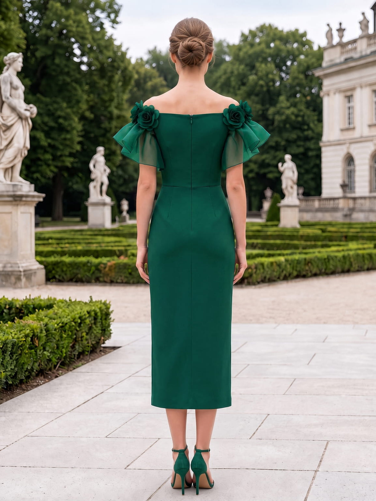 Back view of a tea-length mother of the bride dress featuring a straight off-the-shoulder back neckline, floral shoulder accents, organza flutter sleeves, a fitted satin sheath silhouette, and a center-back zipper.