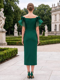 Back view of a tea-length mother of the bride dress featuring a straight off-the-shoulder back neckline, floral shoulder accents, organza flutter sleeves, a fitted satin sheath silhouette, and a center-back zipper.