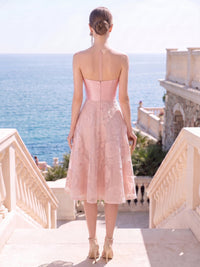 Back view of a blush satin and lace floral mother of the bride dress with sheer upper back detail, slim straps, center-back zipper, and a tea-length A-line skirt with floral lace overlay.