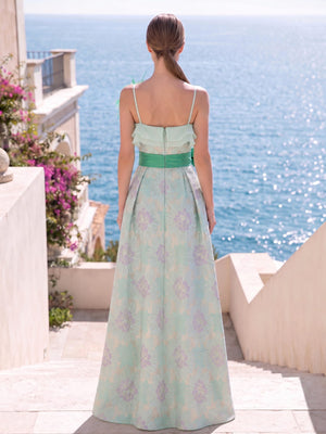 Back view of a floral jacquard satin floor-length mother of the bride gown with slim spaghetti straps, layered ruffle detailing across the upper back, contrasting waistband, center-back zipper, and flowing A-line skirt.