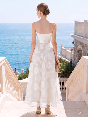 Back view of a floral lace tea-length mother of the bride dress featuring a sheer illusion mesh upper back, fitted structured bodice, defined natural waist, center-back zipper closure, and a softly flared floral lace A-line skirt.