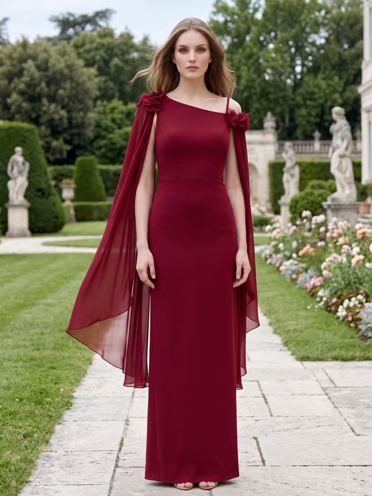 Front view of a wine red chiffon floor-length mother of the bride gown featuring an asymmetric one-shoulder neckline with a slim spaghetti strap on the opposite side, three-dimensional floral shoulder accents, long flowing chiffon cape panels, fitted bodice, sleek column silhouette, and elegant floor-length hem.