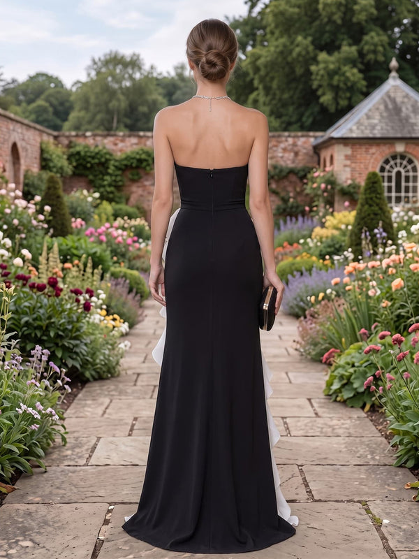 Back view of a black satin floor-length mother of the bride gown featuring a clean straight strapless back neckline, fitted bodice and waist, sleek sheath skirt, subtle white organza ruffle detail along the side, and concealed center-back zipper closure.