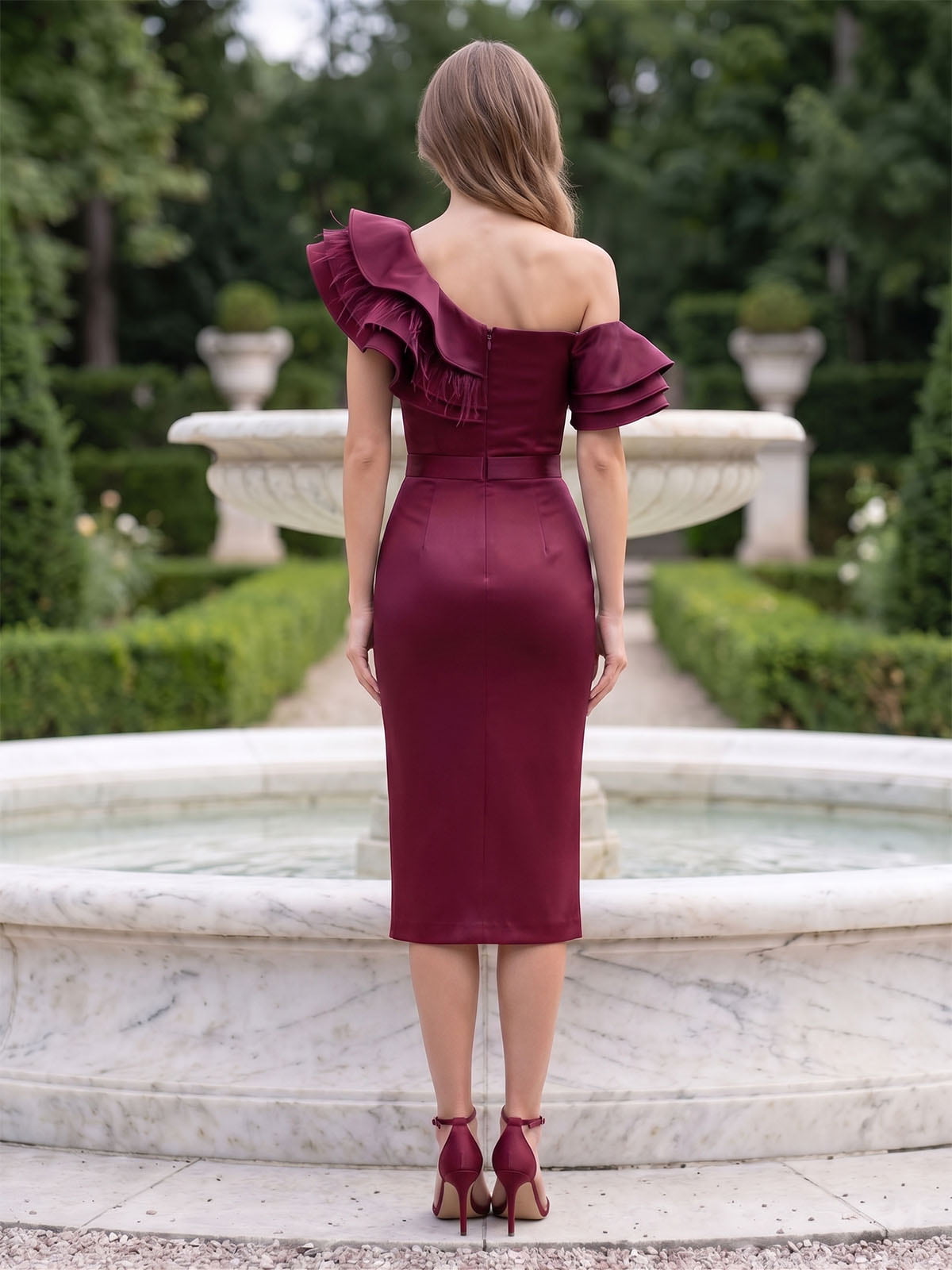 Back view of a burgundy satin knee-length mother of the bride dress with an off shoulder design, layered ruffle detail, concealed center-back zipper, fitted silhouette, and sheath skirt.