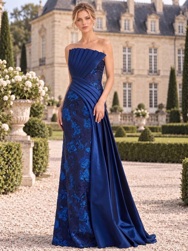 Front view of a floral jacquard satin mother of the bride dress featuring a structured strapless pleated neckline, tonal blue floral jacquard, diagonal pleated waist detail, smooth satin side draping and an elegant floor-length A-line silhouette.