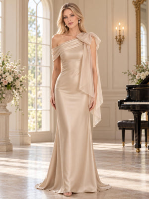 Front view of an elegant faux silk mother of the bride dress featuring a fitted sheath silhouette, asymmetric draped neckline, statement organza shoulder bow, long cascading shoulder drape and graceful floor-length skirt.