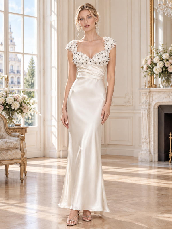 Front view of an elegant ivory faux silk mother of the bride dress featuring a V-neckline framed with dimensional 3D floral appliqués and delicate bead accents, sleeveless shoulders, softly pleated waist and a fitted floor-length sheath silhouette.