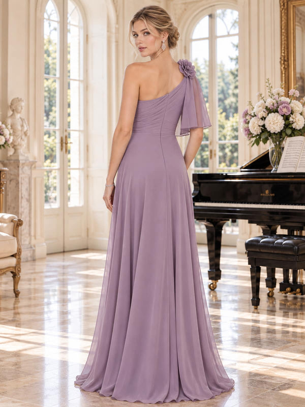 Back view of a dusty lavender chiffon mother of the bride dress featuring an asymmetric one-shoulder bodice, dimensional shoulder flower, flowing chiffon cape overlay, fitted waist and floor-length A-line skirt.