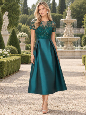 Front view of an emerald green mother of the bride dress featuring a sheer illusion round neckline, short sleeves, intricate beaded floral lace bodice and a structured pleated satin A-line tea-length skirt.